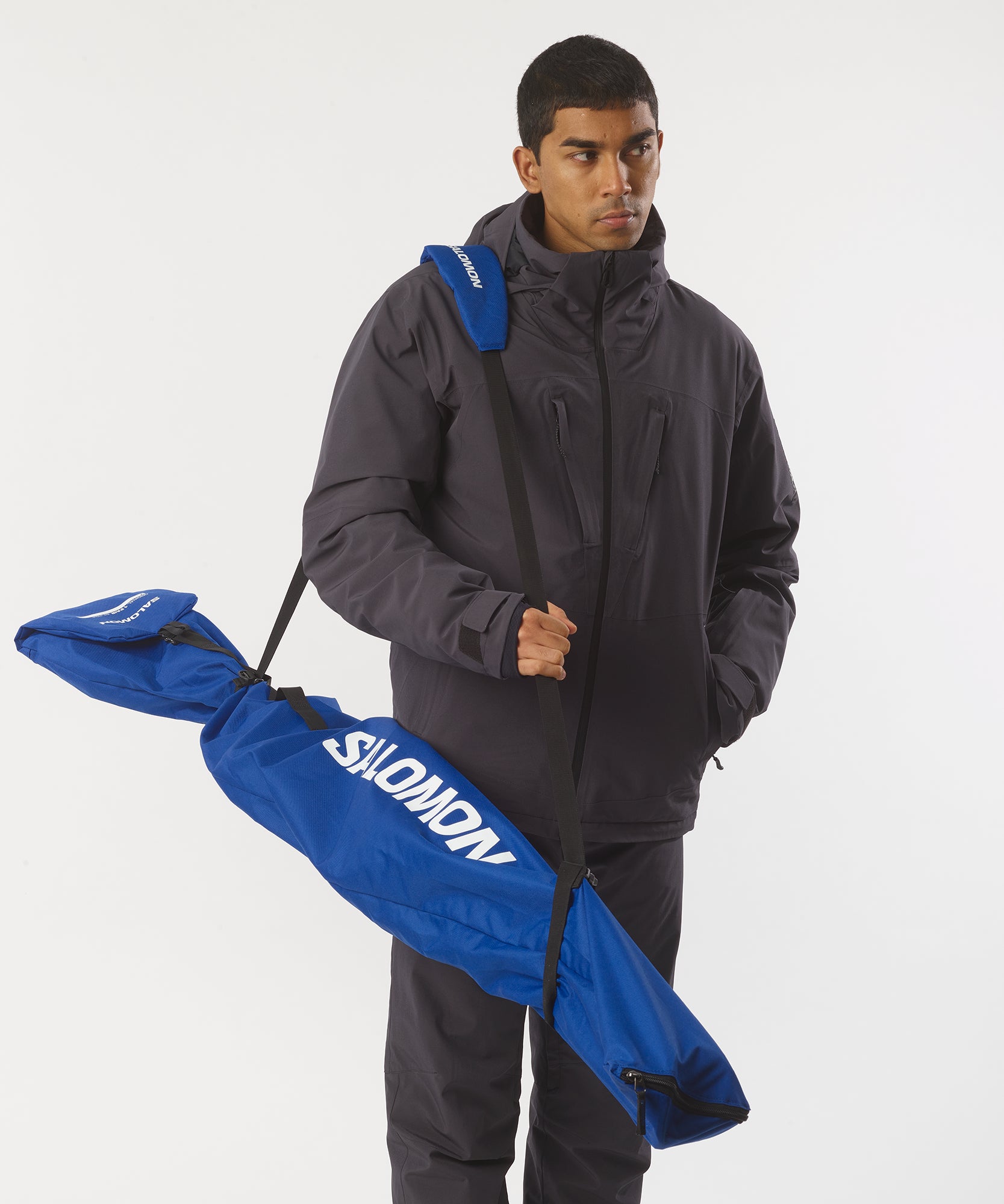 Homme portant un sac de ski : sac de ski bleu Salomon sur l'épaule, porté par une personne en tenue d'hiver.