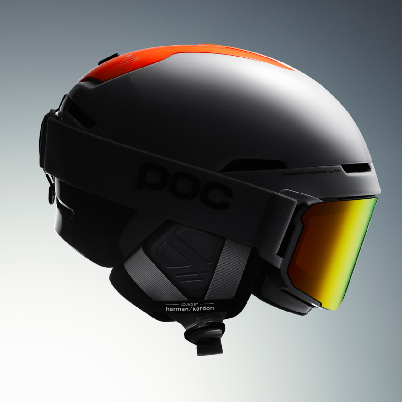 Grauer Skihelm mit Akzenten Grauer Skihelm mit orangefarbenem Akzent, schwarzem Brillenband und gelb-goldener Linse, seitliche Ansicht.