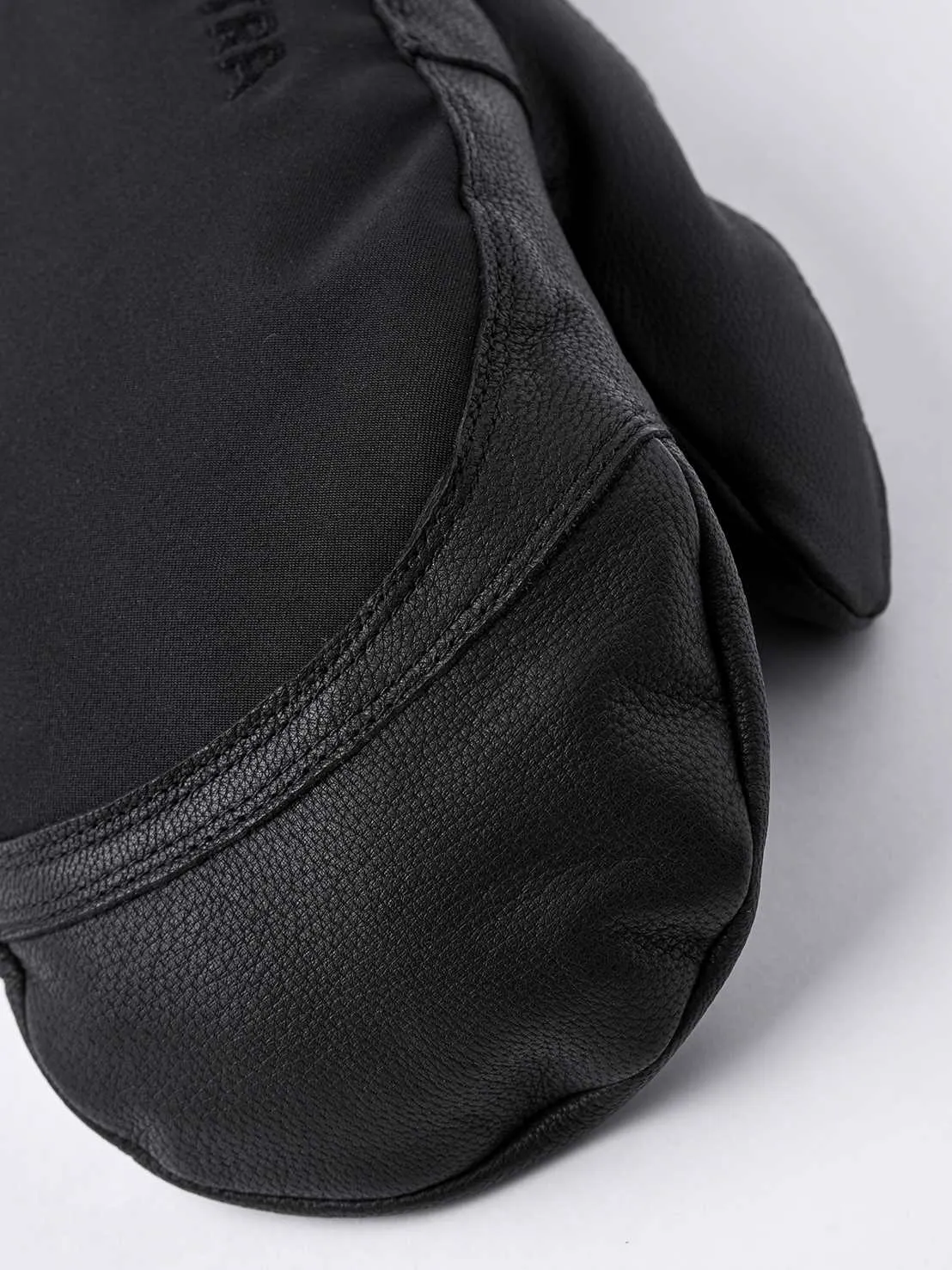 Primo piano di una muffola Hestra Army Leather Extreme Mitt in nero. Pelle sul palmo, tessuto sul dorso della mano.