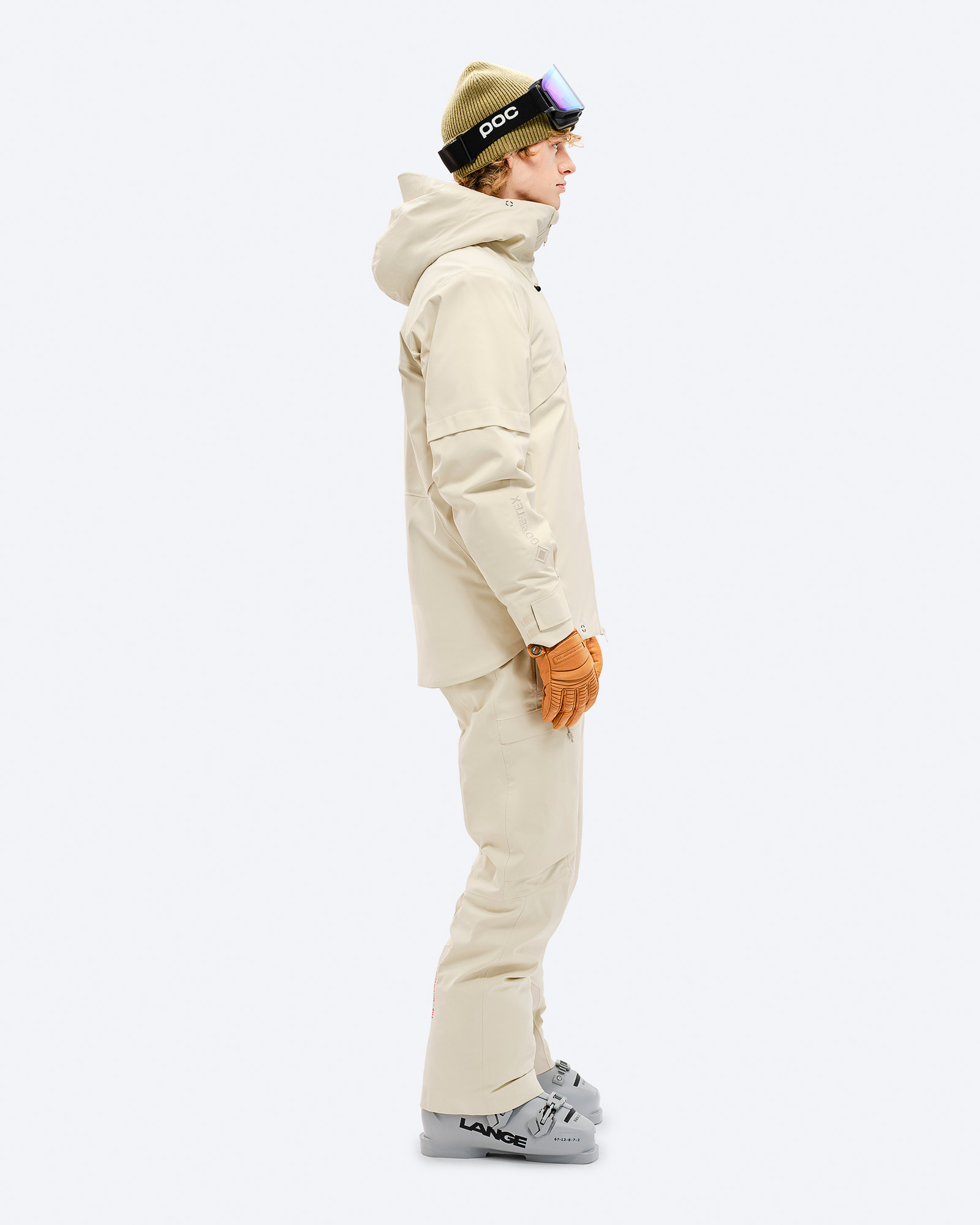 Person in beiger GORE-TEX 2L Stretch Jacke, Hose, Skibrille und Skischuhen, Seitenansicht.