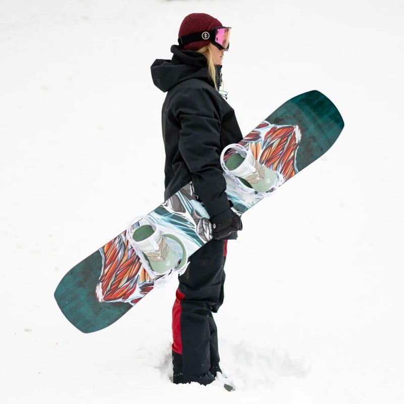 Snowboardfahrende Frau Frau mit Snowboard Twin Sister im Schnee. Sie trägt Winterkleidung und Skibrille.
