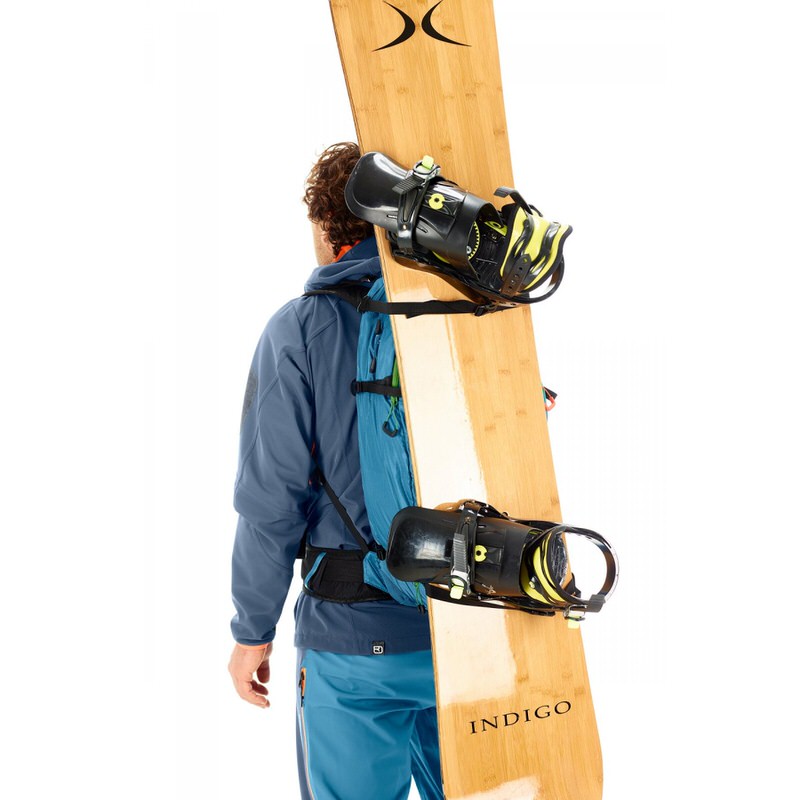 Sac à dos bleu avec snowboard Personne avec un sac à dos Ascent 32 bleu et un snowboard fixé en diagonale.