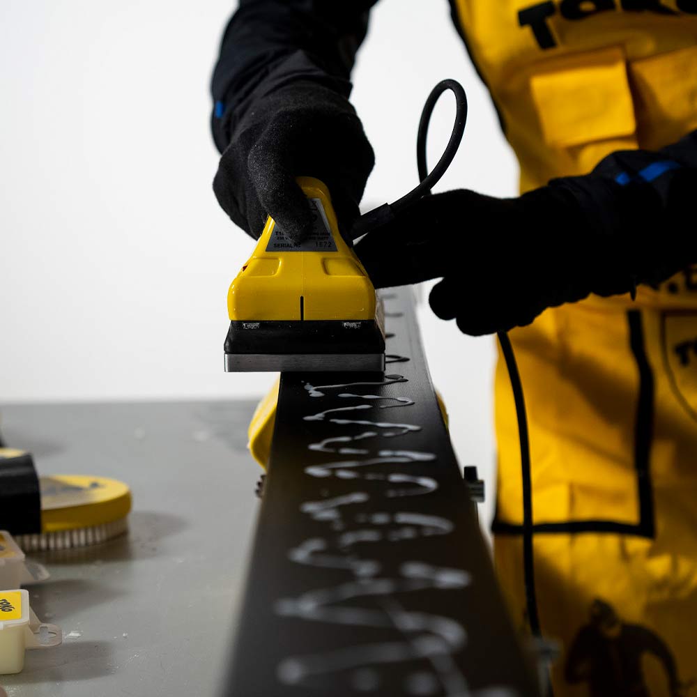 Ski Wachsen mit Bügeleisen Eine Person wachst einen Ski mit einem gelben Bügeleisen, weiße Wachstropfen sind auf dem schwarzen Ski zu sehen.