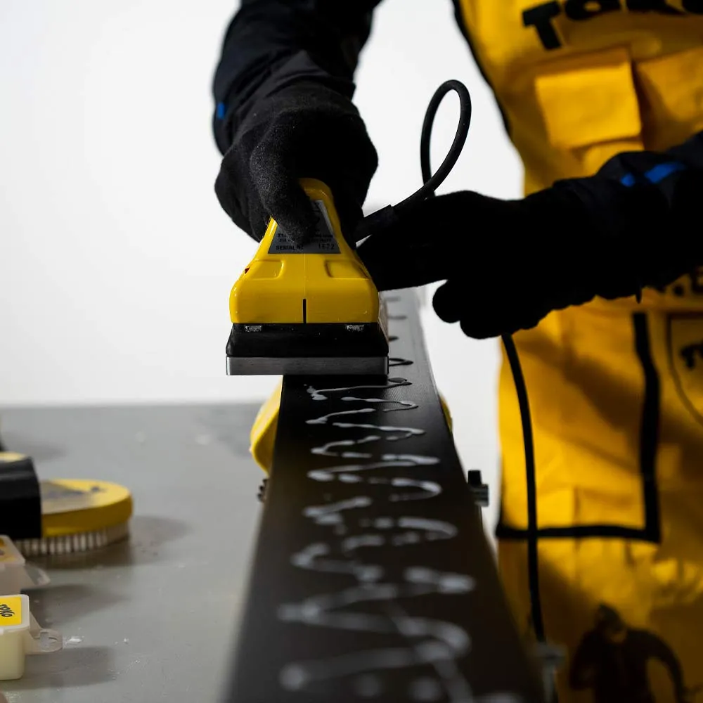 Une personne cire un ski avec un fer à repasser jaune, des gouttes de cire blanche sont visibles sur le ski noir.