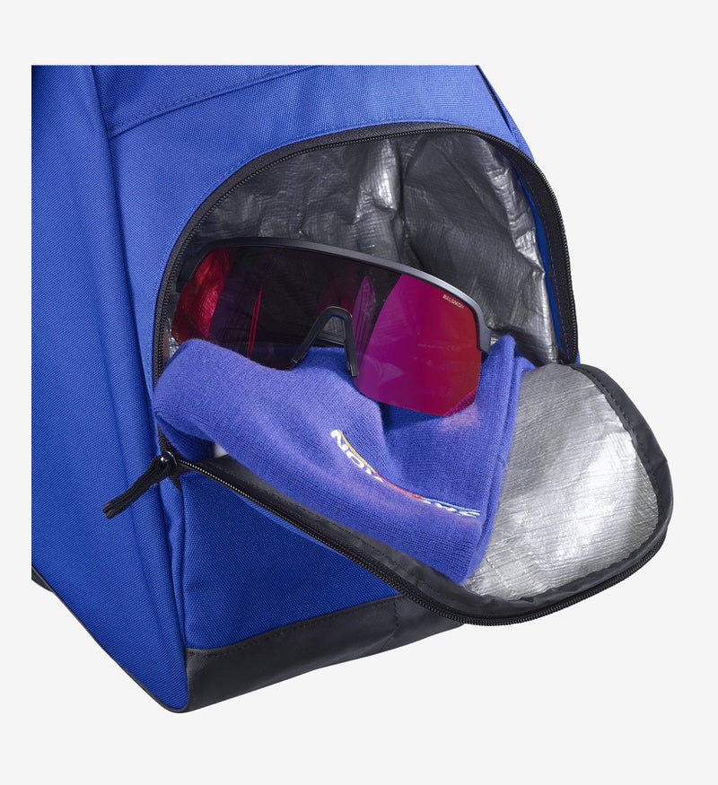 Sac à chaussures de ski bleu, compartiment ouvert avec des lunettes de soleil sur un tissu bleu.