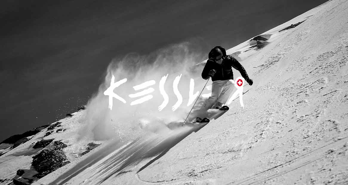 Schwarzweißaufnahme eines Skifahrers in Bewegung auf einer verschneiten Piste, Schnee stäubt hinter ihm auf. Der Schriftzug "Kessler" ist im Bild integriert.
