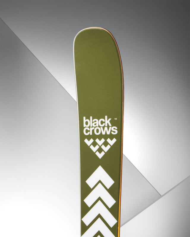 Ein olivgrüner Ski mit weißem "black crows"-Logo und Pfeilen vor einem grauen Hintergrund.