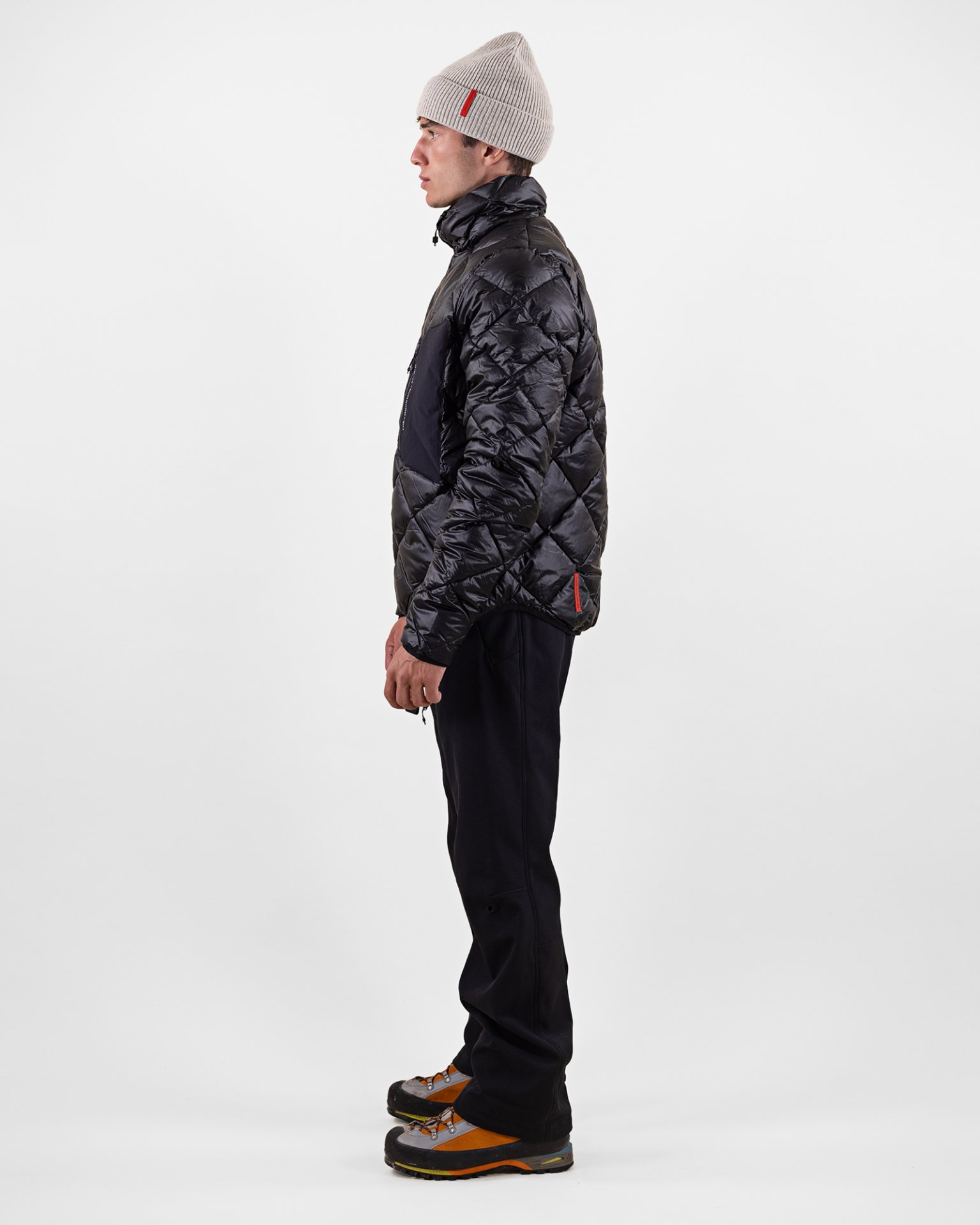 Homme en doudoune Un homme vu de profil porte une doudoune noire D-8 T Pertex Techno, un pantalon et une casquette sur un fond blanc.
