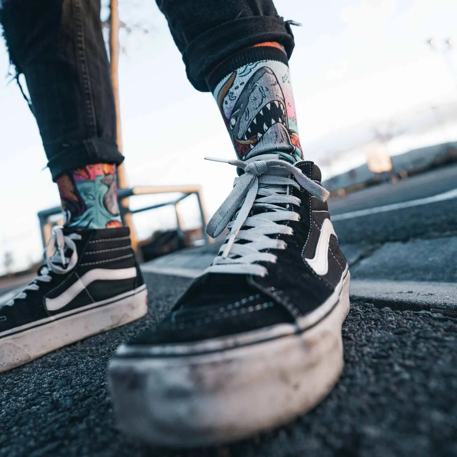Une personne portant un jean noir et des chaussures noires porte des chaussettes "Seamonsters - Mid High" à motif requin.