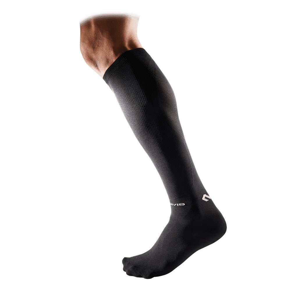 Ein Bein mit einer schwarzen McDavid Elite Recovery Kompressionssocke vor einem weißen Hintergrund.
