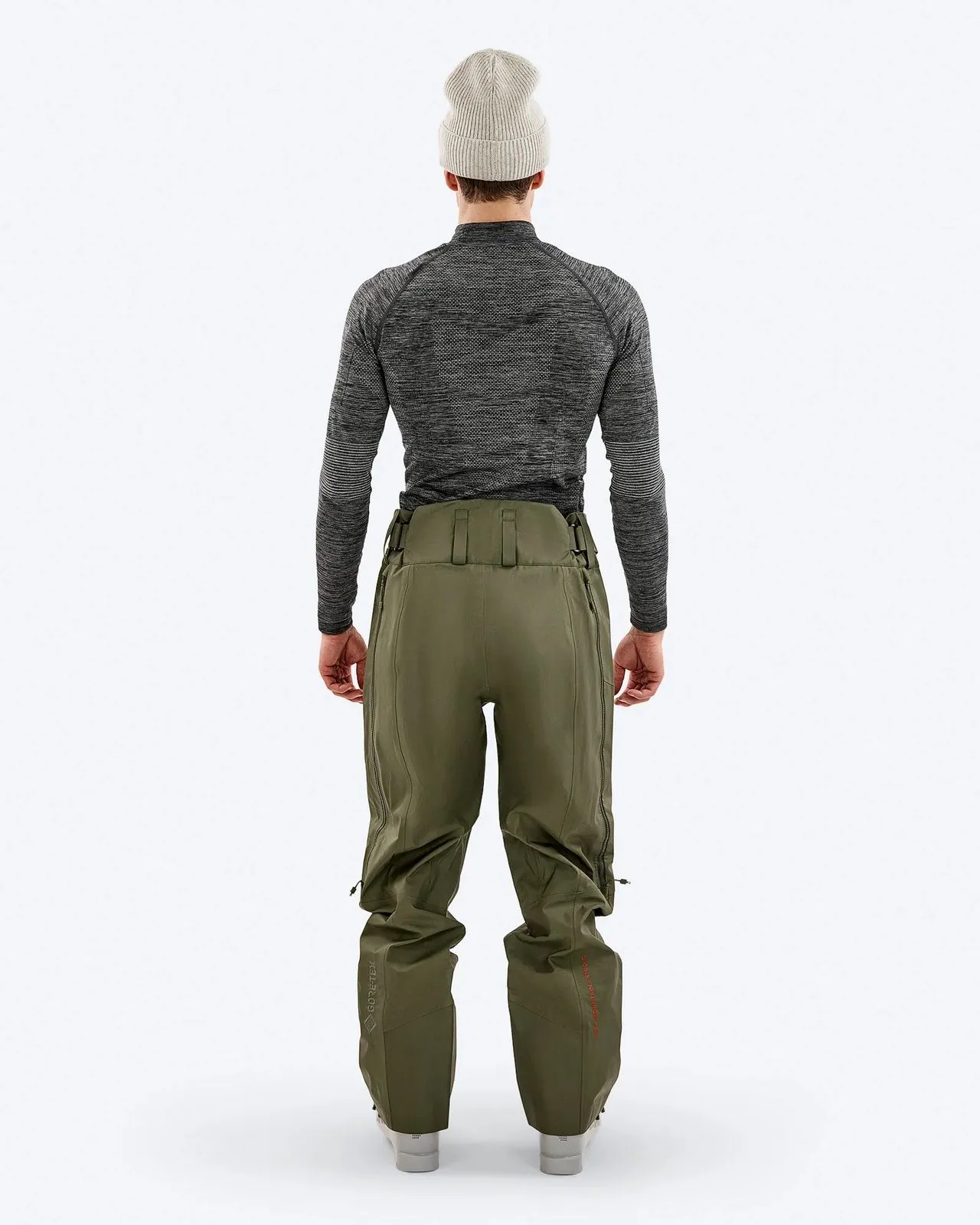 A man from behind, wearing a gray cap, a gray long-sleeved shirt and olive green trousers. The trousers have zippers on the sides.