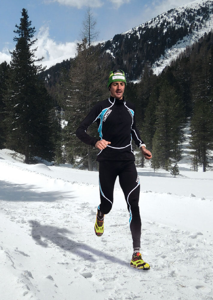 Schnee Läufer mit Schuhkrallen Läufer mit Corsa Schuhkrallen läuft im Schnee vor einem Berg.