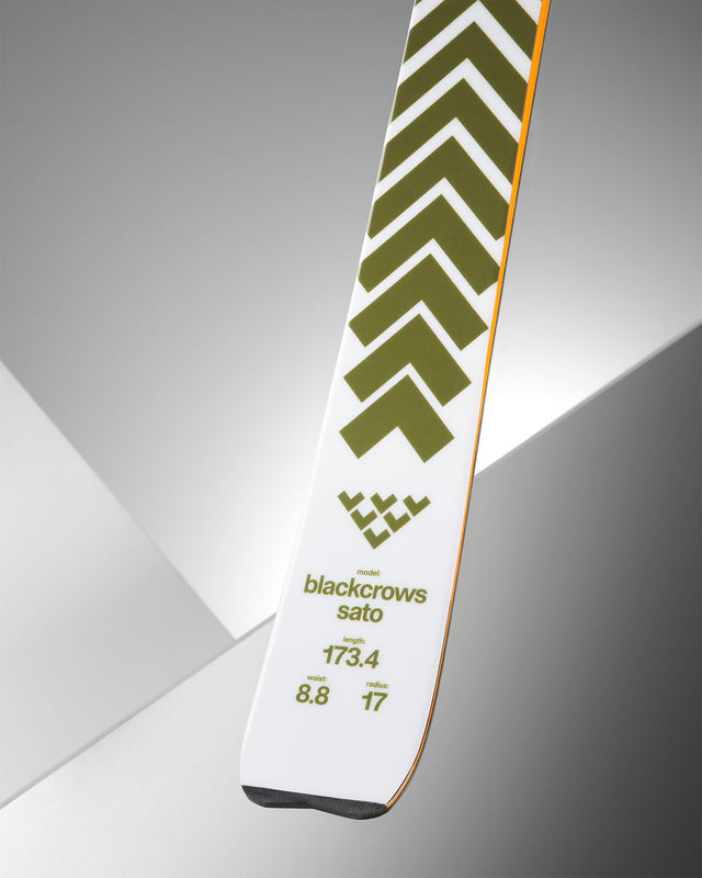 Nahaufnahme eines Skis mit grünem Chevron-Muster auf weißem Grund, Modellname "blackcrows sato" und technischen Daten.