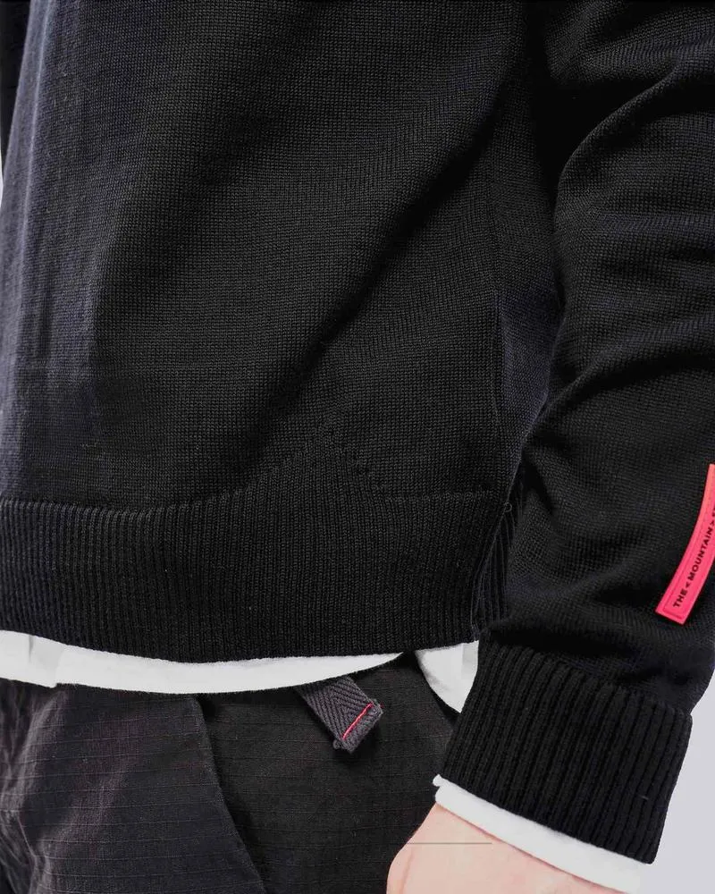 Nahaufnahme eines schwarzen K-3 Ski Pullovers aus Merinowolle mit Rundhalsausschnitt und rotem Etikett.