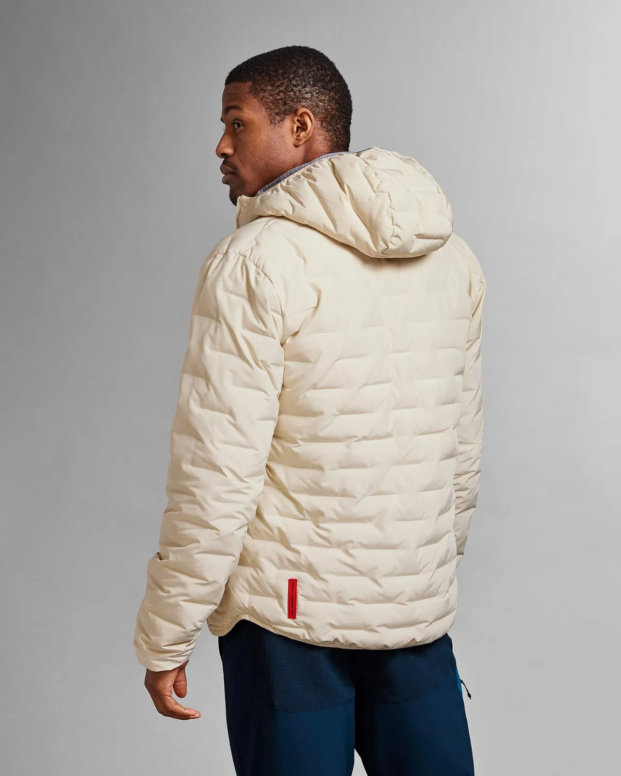 Person from behind in a reversible, light beige hooded jacket ("Castle Wall") with blue pants against a light background.