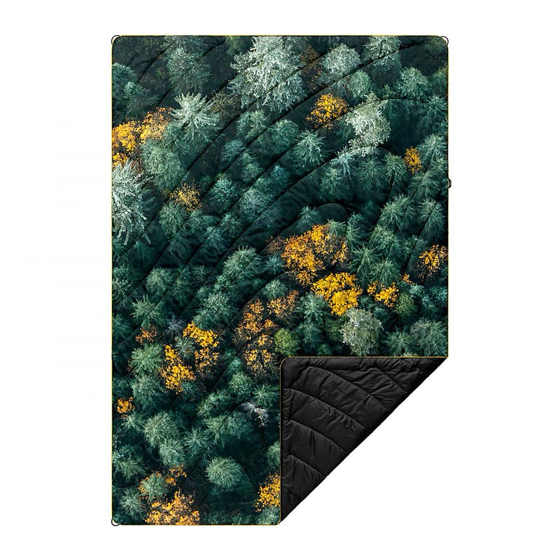 Puffy Blanket mit Waldmuster; grüne, goldene und weiße Baumkronen von oben. Eine Ecke ist umgeschlagen und zeigt schwarzes Futter.