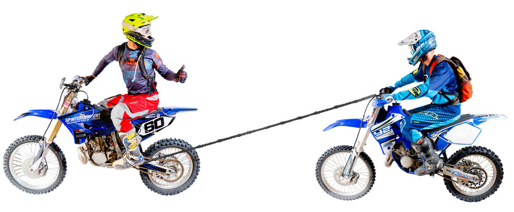 Zwei Motocross-Fahrer auf Motorrädern, durch ein Abschleppseil verbunden. Ein Fahrer gibt einen Daumen nach oben.