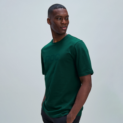 Ein junger Mann mit dunkler Hautfarbe trägt ein grünes T-Shirt mit kurzen Ärmeln und blickt über seine Schulter.