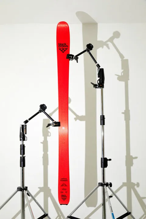 Ski rouge Black Crows Camox Freebird, fixé à des trépieds devant un mur blanc.