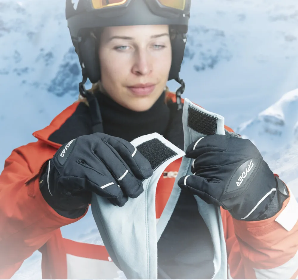 Frau mit Helm und Handschuhen schliesst hellblaue HeiQ Filter Bandana goSnow mit Klettverschluss vor schneebedeckter Bergkulisse.