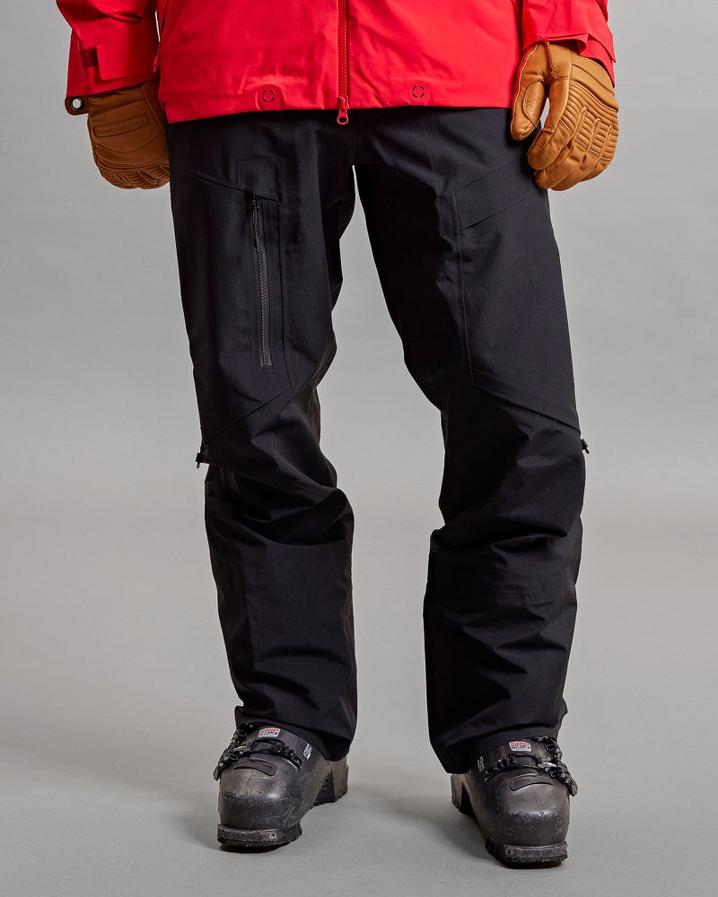 Schwarze GORE-TEX Skihose Vorderansicht einer schwarzen Y-1 HD GORE-TEX Pro 3L Shell Pant mit Skischuhen und Skihandschuhen auf grauem Hintergrund.