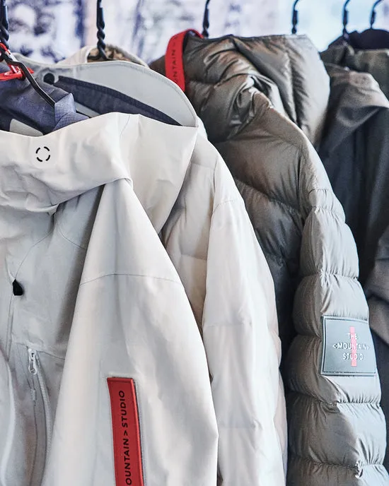 Diverse giacche invernali di colore bianco, grigio e kaki sono appese su grucce. Le etichette rosse sono visibili.