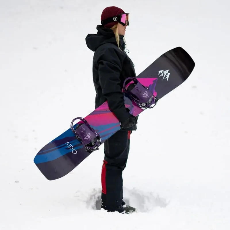 La femme tient Jones Airheart 2.0 Snowboard avec un design coloré dans la neige.
