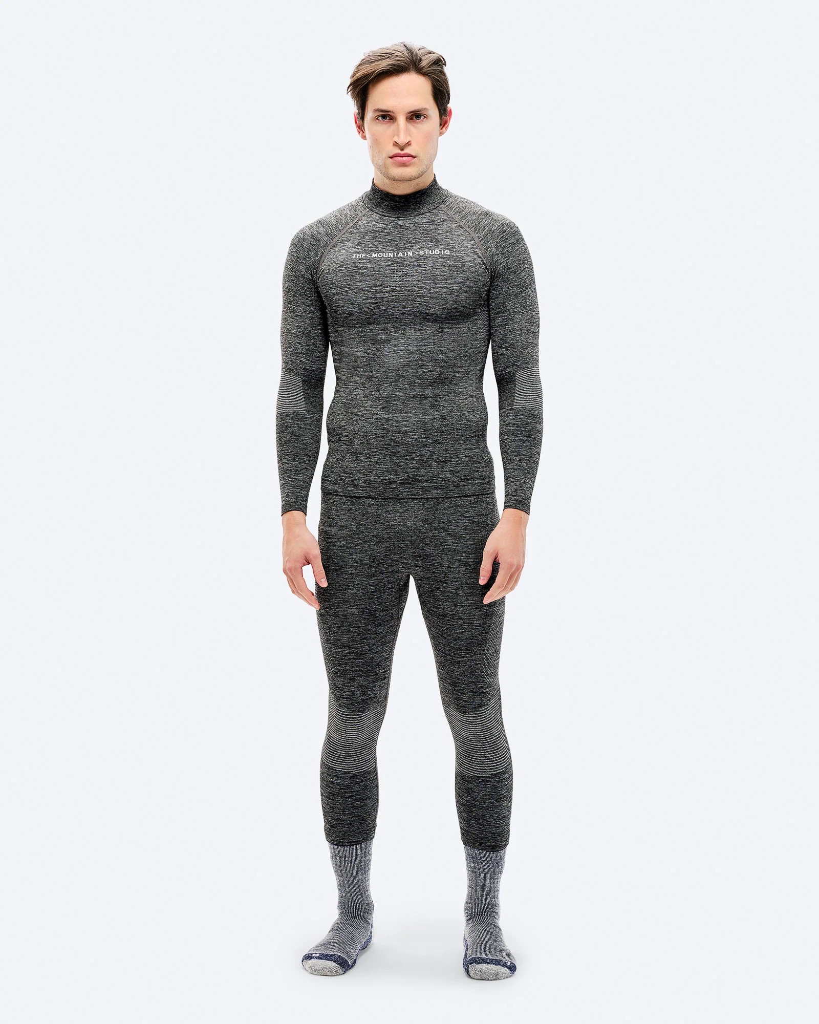 A man in gray sports underwear and socks stands in front of a white background.