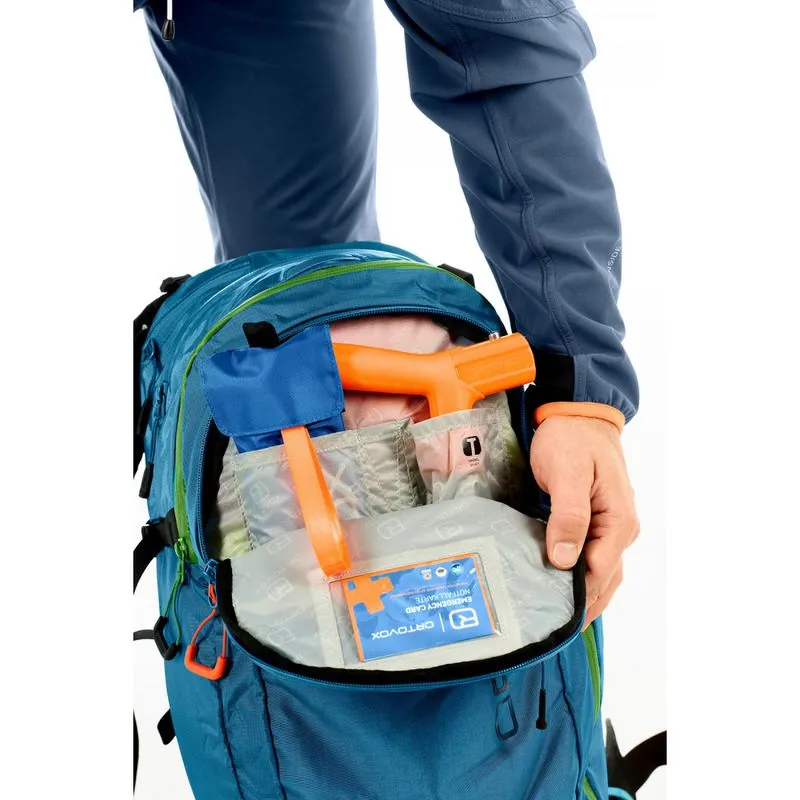 Primo piano: zaino Ortovox Ascent 32 blu aperto, pieno di attrezzatura e di una carta di emergenza.