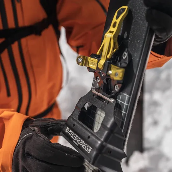 Close-up of an ATK crampon attached to a ski binding, held by a person wearing gloves.