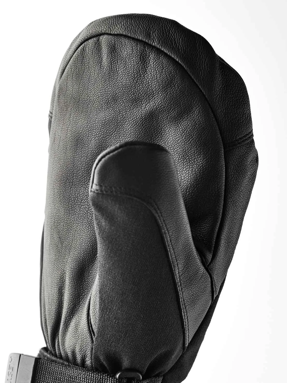 Une moufle en cuir noir est posée sur une surface blanche. Le pouce est tourné vers l'avant et le dos de la main est bombé.
