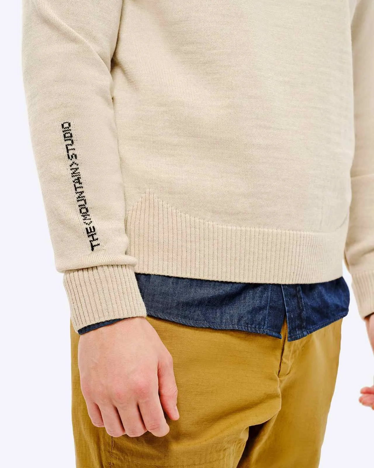 Vista dettagliata del maglione da sci St. Moritz, beige, con scritte sulle maniche, su camicia blu e pantaloni beige.