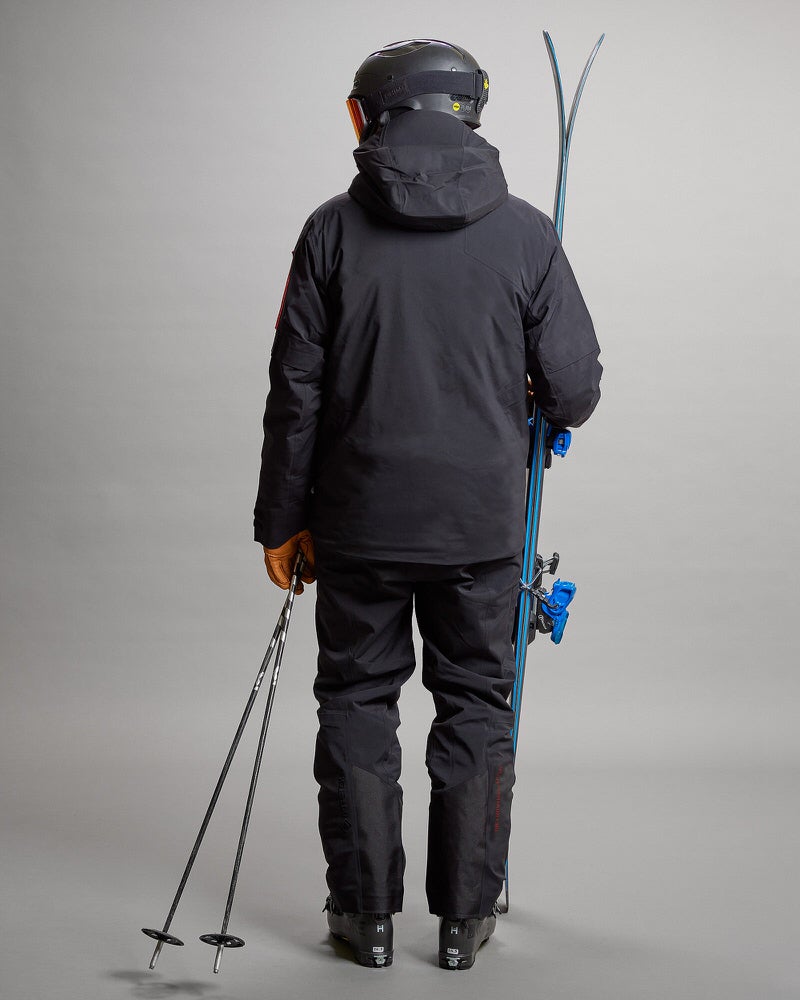 Skieur en Gore Tex Personne de dos avec skis, bâtons, casque et veste et pantalon noirs S-1 Gore Tex 2L Stretch Insulated.