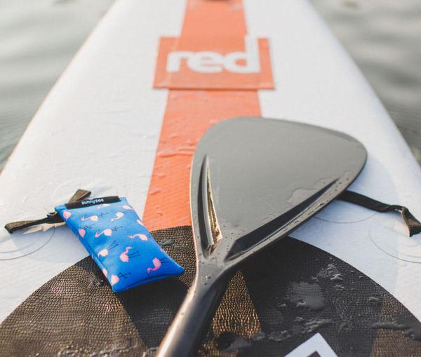 Fenicottero blu sunnysoc su tavola da surf con pagaia. Occhiali da sole di protezione.