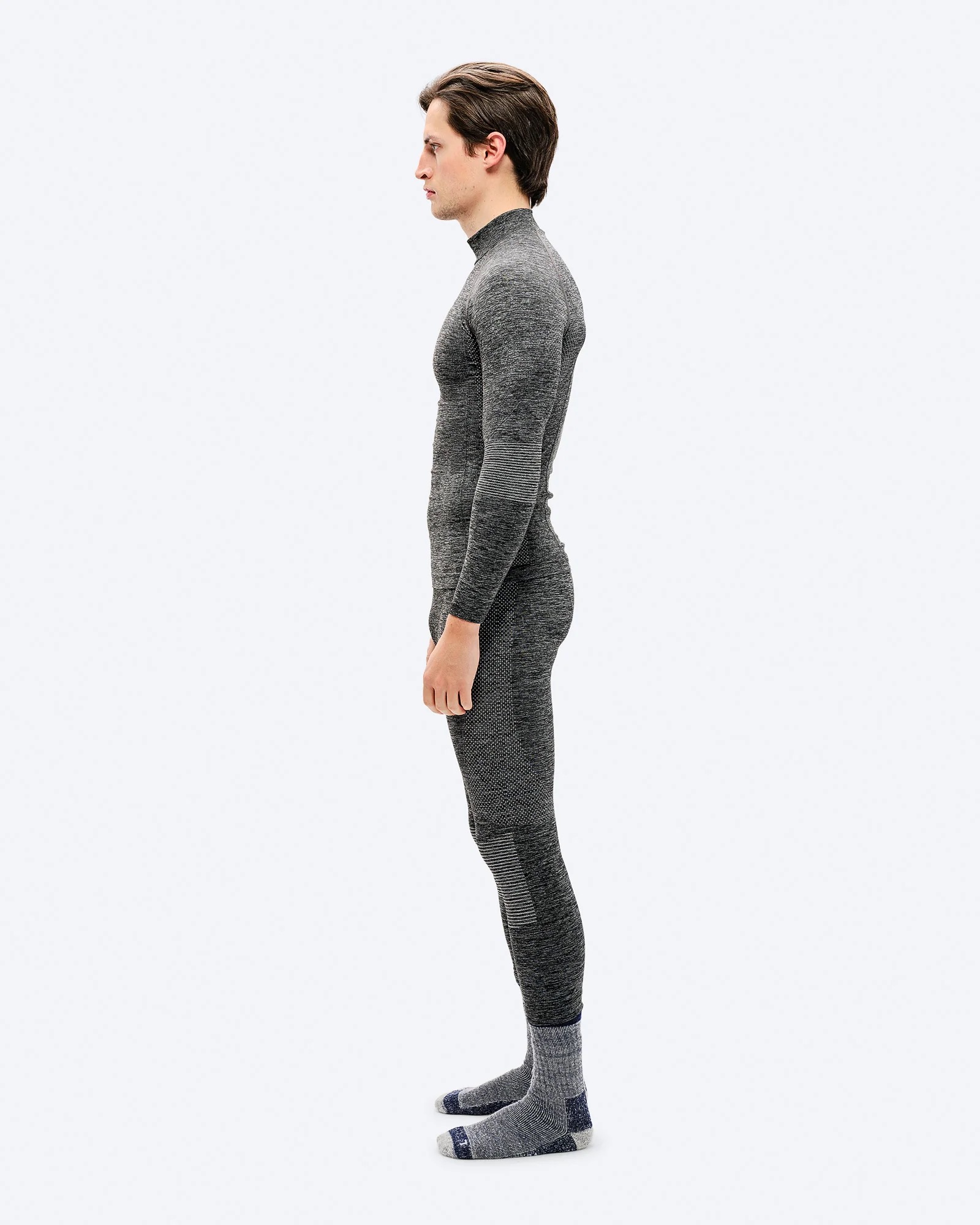 Man in gray, tight-fitting sportswear in profile against a white background. He is wearing gray socks.