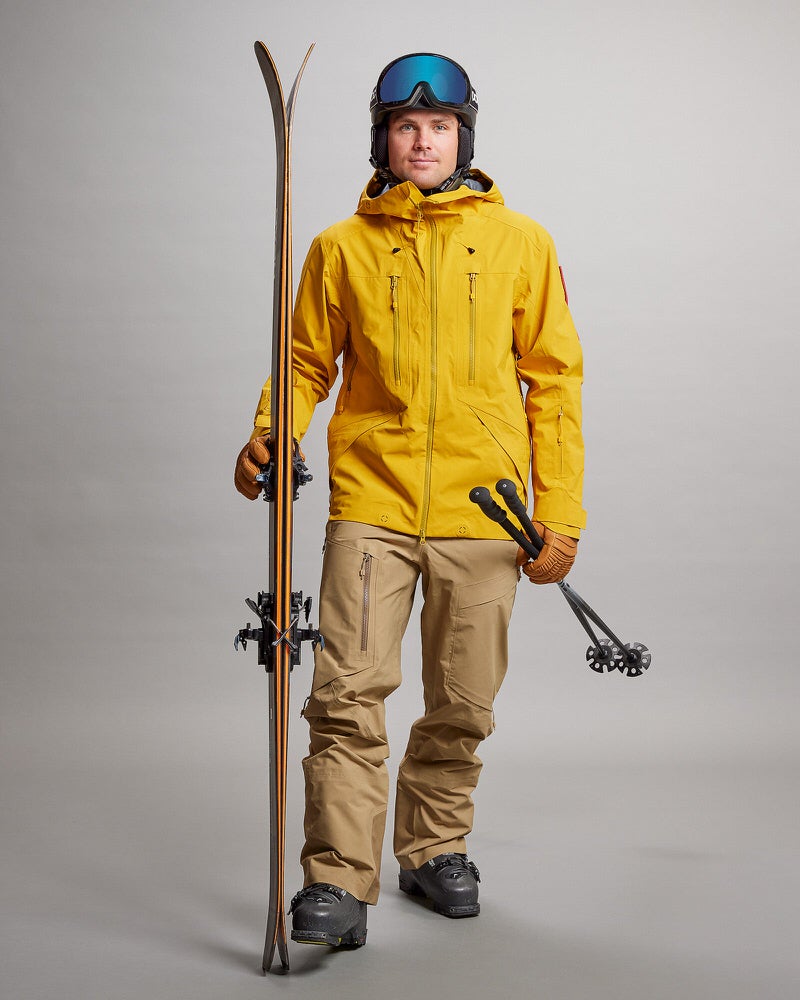 Skifahrer mit GORE-TEX Mann in Skikleidung mit GORE-TEX Pro Hose, gelber Jacke, Helm und Skiern.