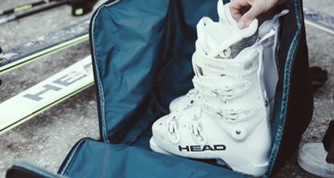 Un sac à chaussures de ski ouvert avec une chaussure de ski blanche de la marque HEAD, des skis et des bâtons de ski sont posés à côté.