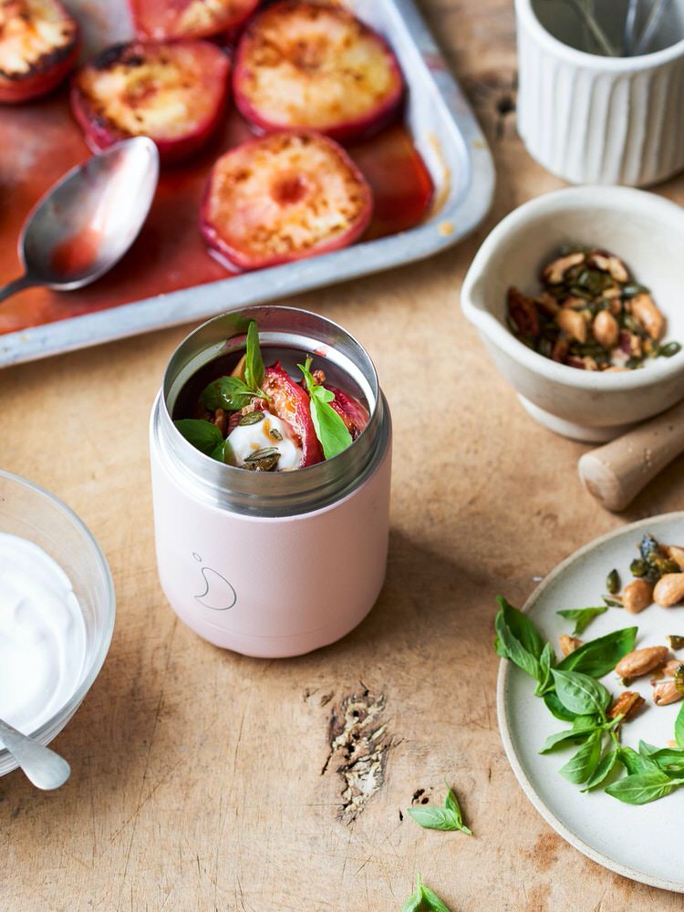 Rosa Chillys Food Pot mit Mahlzeit und Zutaten auf einem Holztisch. Im Hintergrund ein Blech mit gegrillten Pfirsichen.