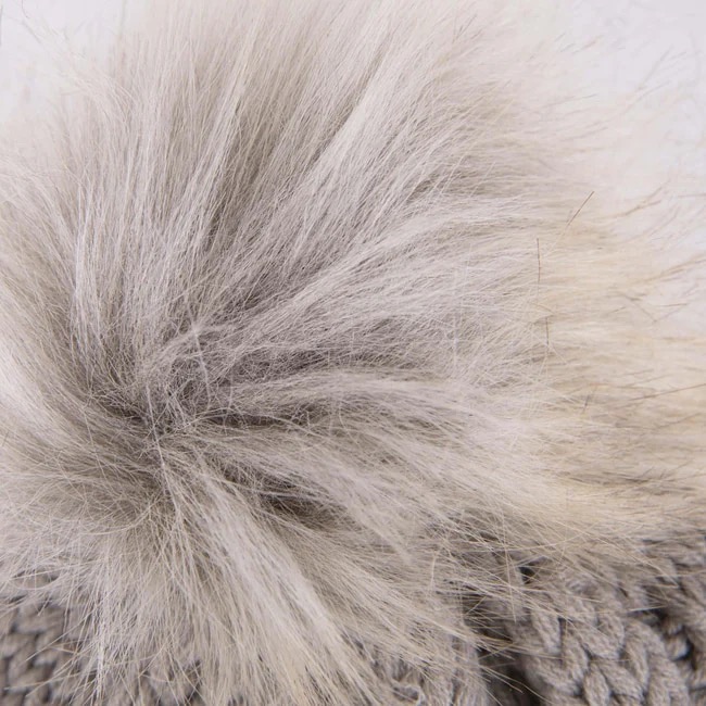 Détail d'un bonnet tricoté gris avec un grand pompon touffu dans les tons de gris et de blanc.