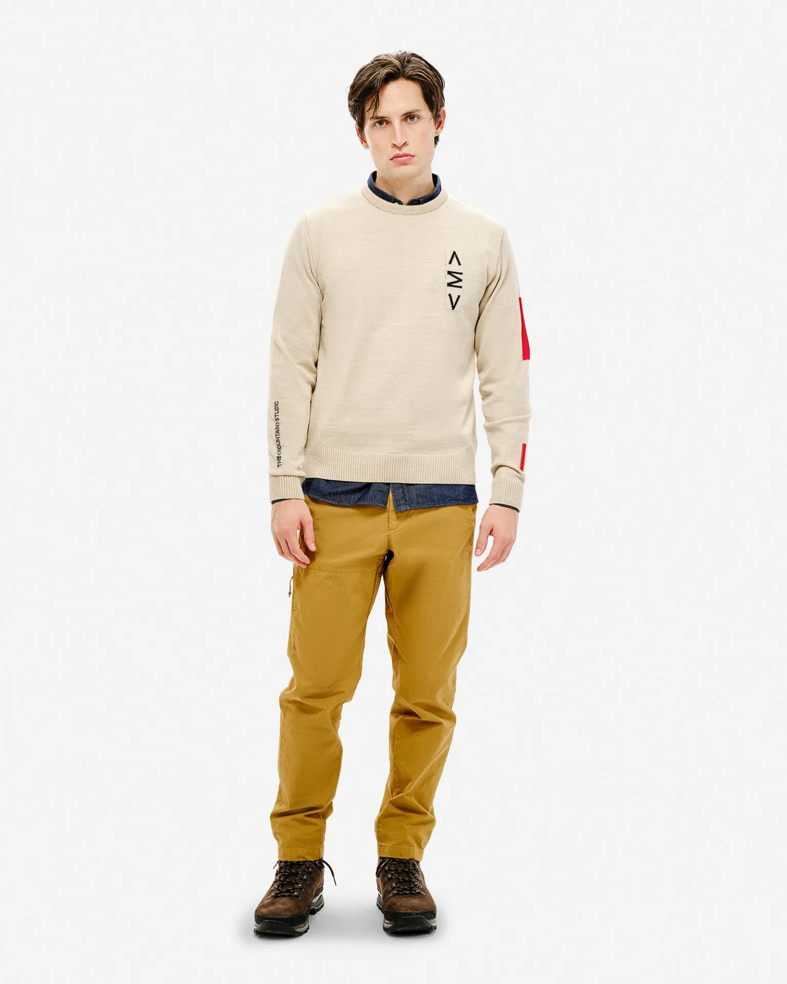 Uomo con maglione da sci beige con motivo, pantaloni e scarpe marroni su sfondo bianco.