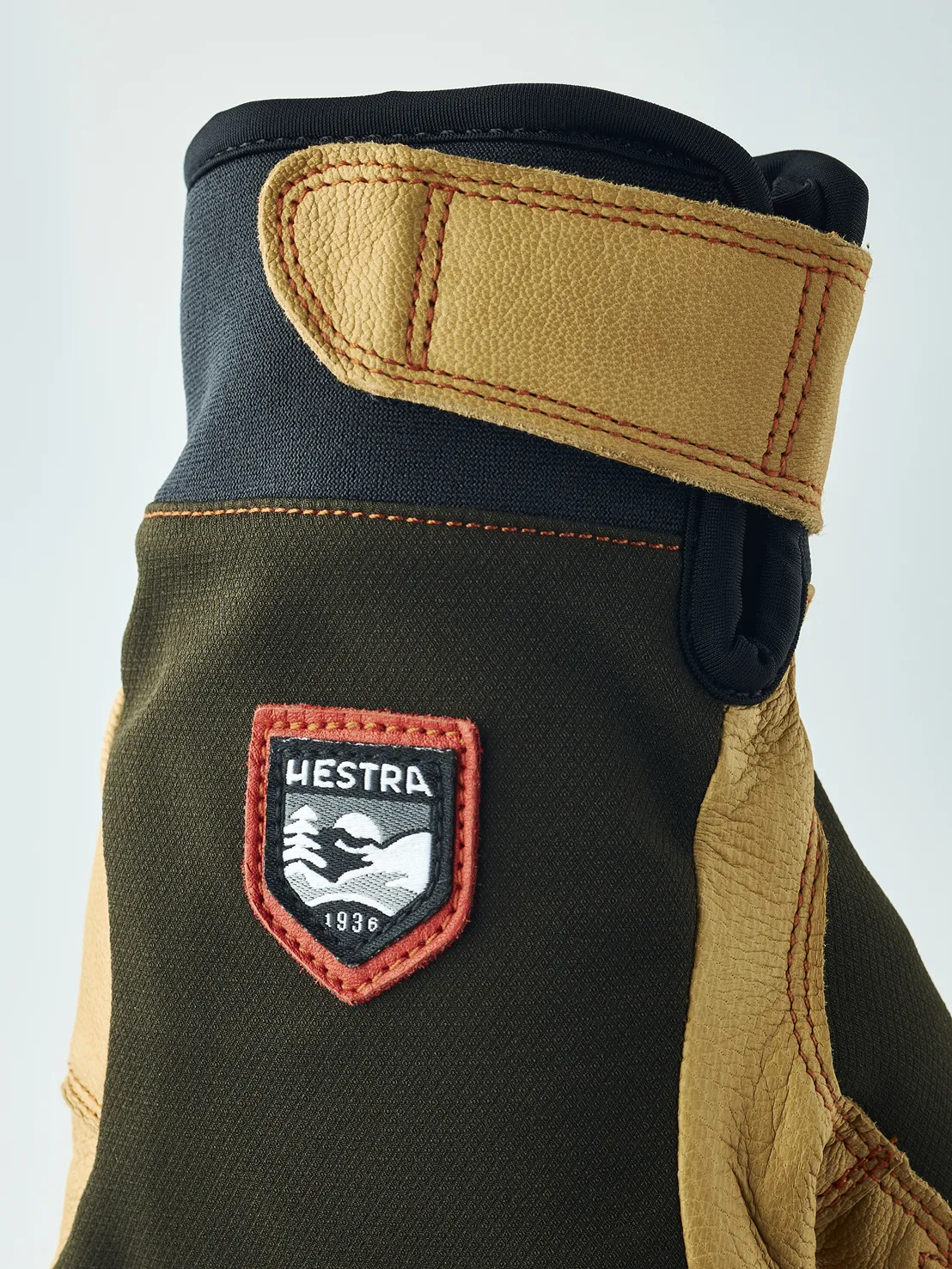 Détail d'un gant avec dessus marron, détails en cuir et logo "Hestra 1936". Le gant a une manchette avec fermeture velcro.