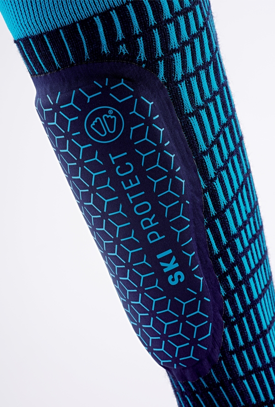 Nahaufnahme von Sidas Ski Protect Skisocke mit Schienbeinschutz, blauen geometrischen Mustern und "SKI PROTECT" Schriftzug.