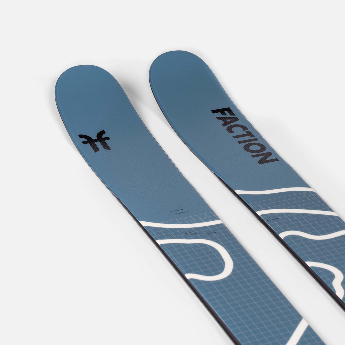 Blau-graue Ski der Marke Faction mit geometrischem Muster und Schriftzug liegen auf einem weißen Untergrund.