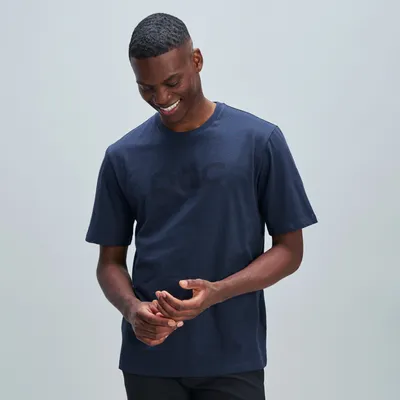 Ein lächelnder, dunkelhäutiger Mann trägt ein dunkelblaues T-Shirt mit dem Schriftzug "poc" und berührt seine Hände.
