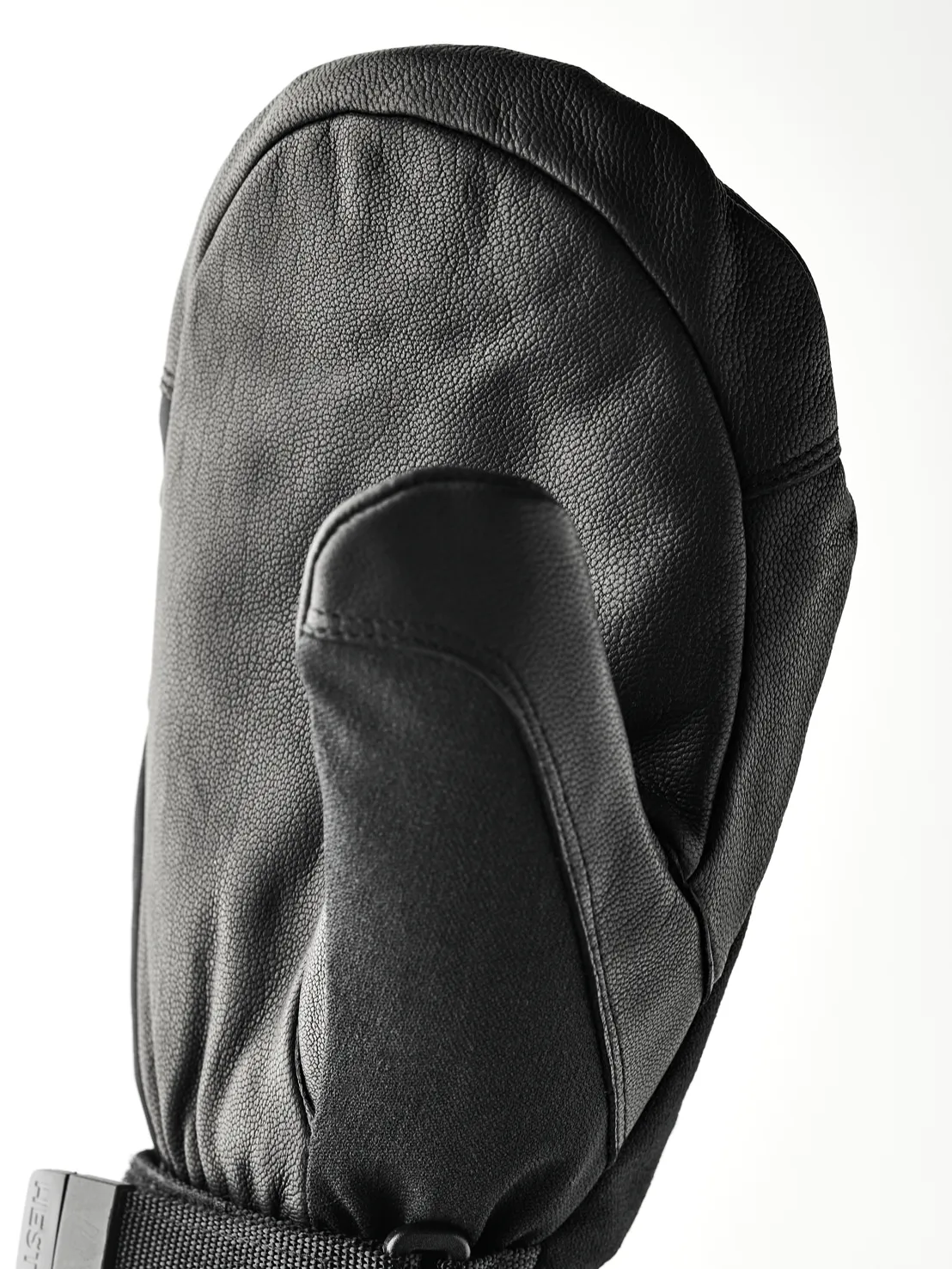 Une moufle en cuir noir est posée sur une surface blanche. Le pouce est tourné vers l'avant et le dos de la main est bombé.