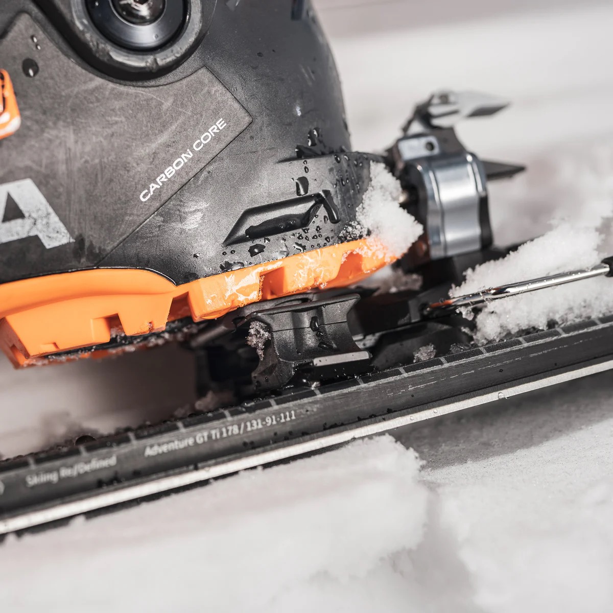 Nahaufnahme eines Skischuhs mit Carbonkern, befestigt auf einem Ski im Schnee.
