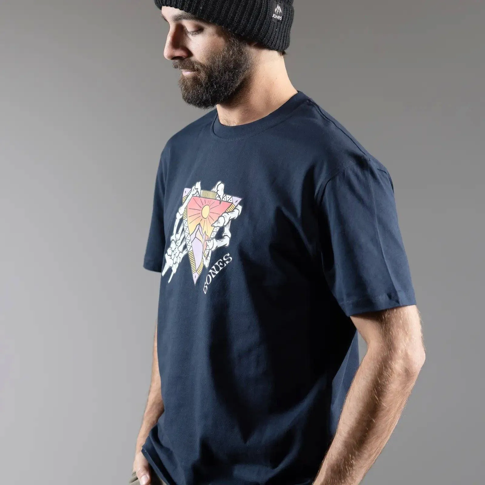 Mann mit Mütze trägt Jones Organic Cotton Tee mit Grafik eines Dreiecks und Skeletthänden.