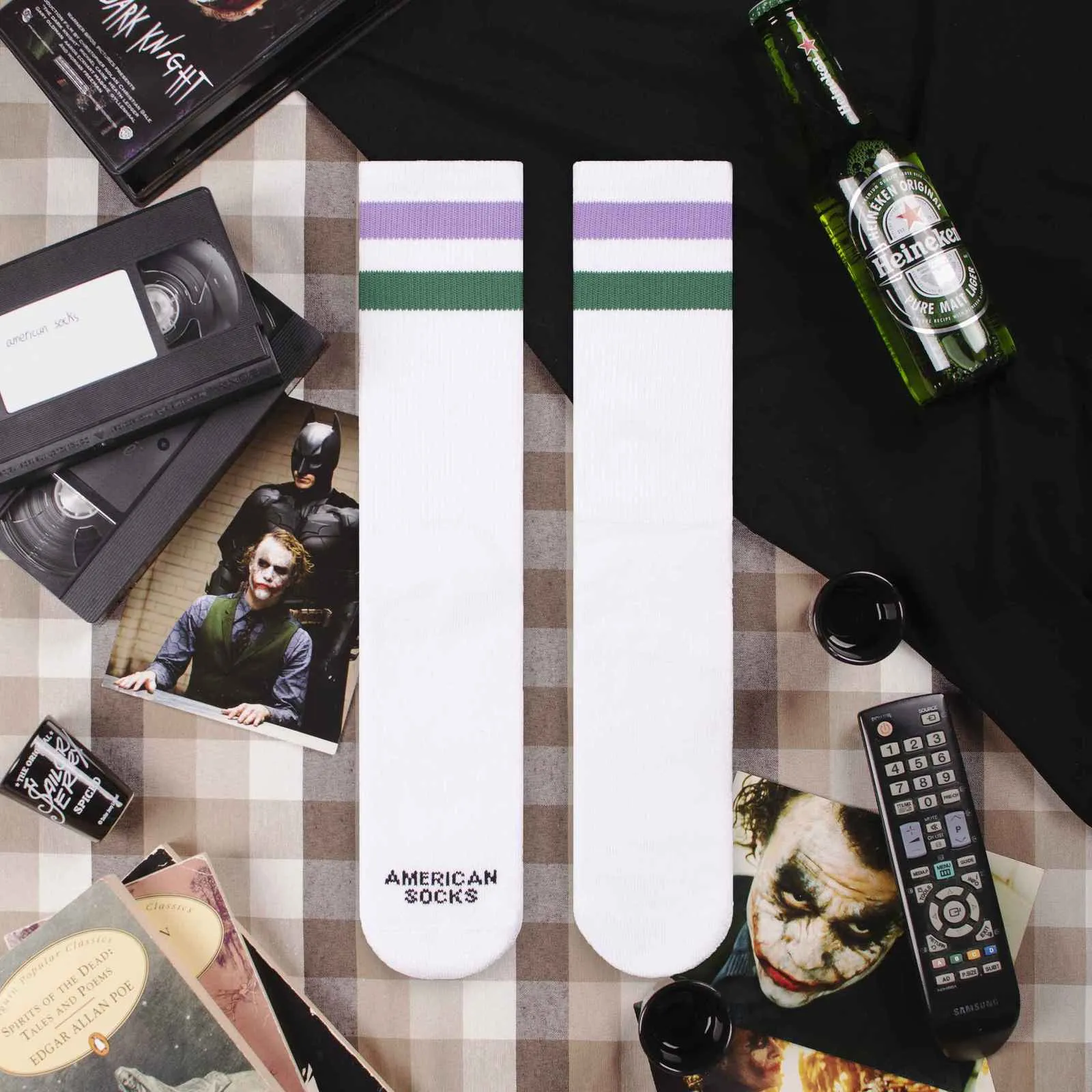 Weiße Mid High Socken mit lila und grünem Streifen liegen auf einem karierten Tuch. "American Socks" Schriftzug ist zu sehen.