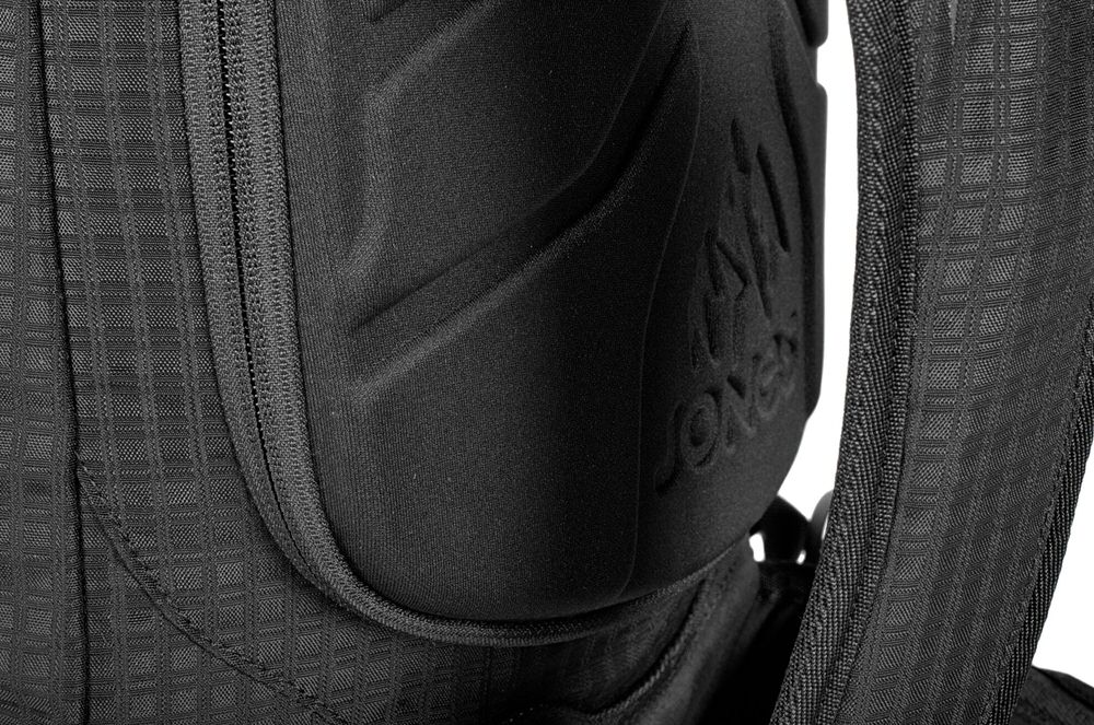 Jones DSCNT Rucksack Detailansicht: Jones DSCNT RAS Rucksack, schwarzes Textil mit Reißverschluss und gepolstertem Tragebereich mit Firmenlogo.