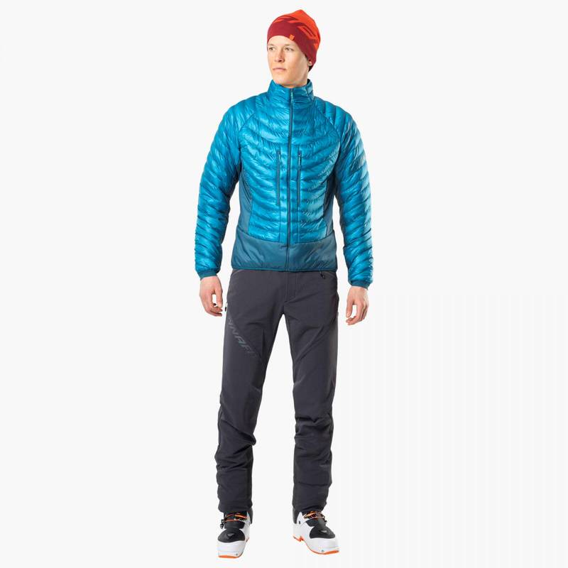 Mann in Skitourenhose TLT Touring DST PNT, blauer Jacke, roter Mütze, vor weißem Hintergrund.